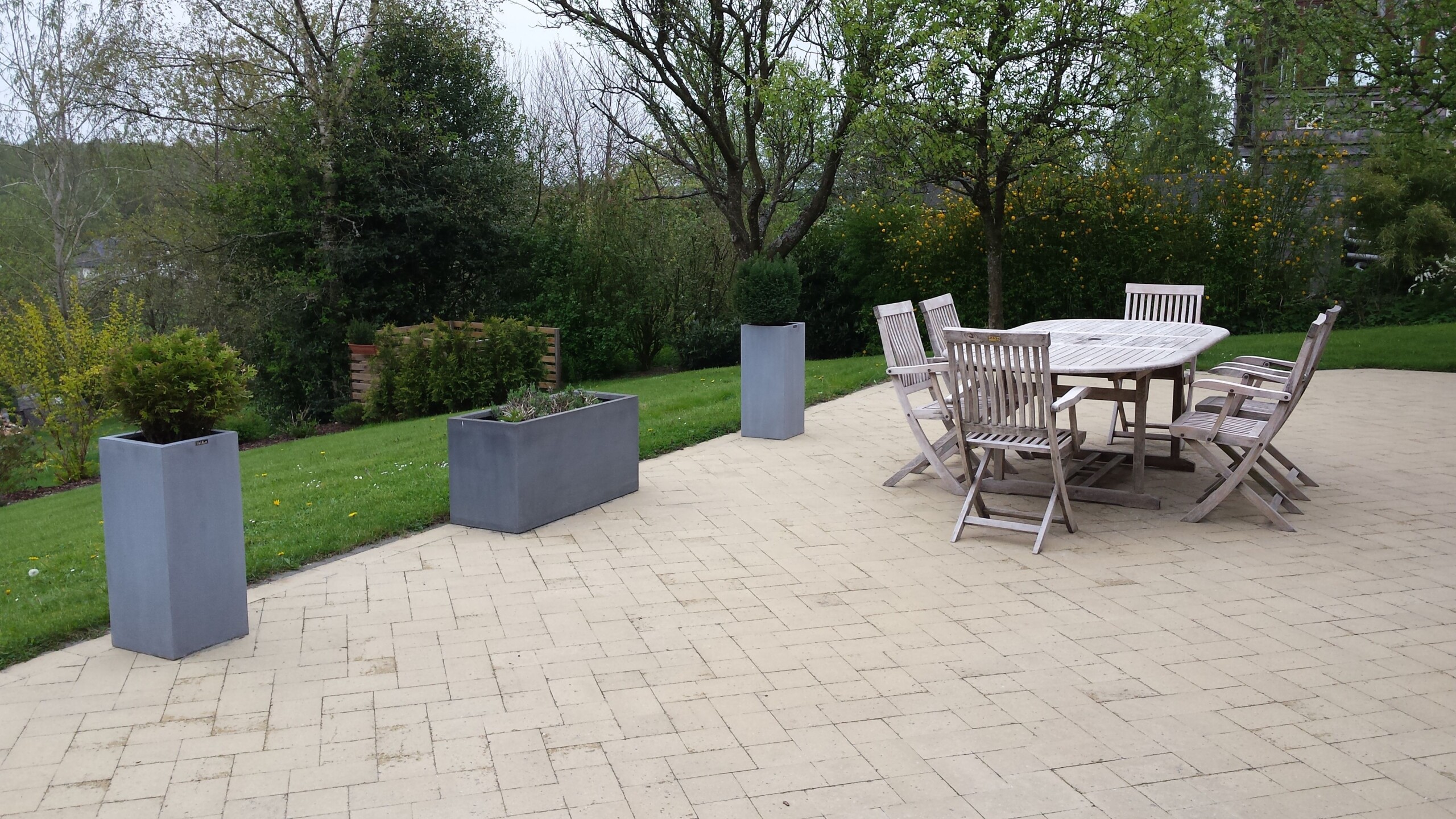 Une terrasse en pavés de béton gris, aménagée avec une table et des chaises