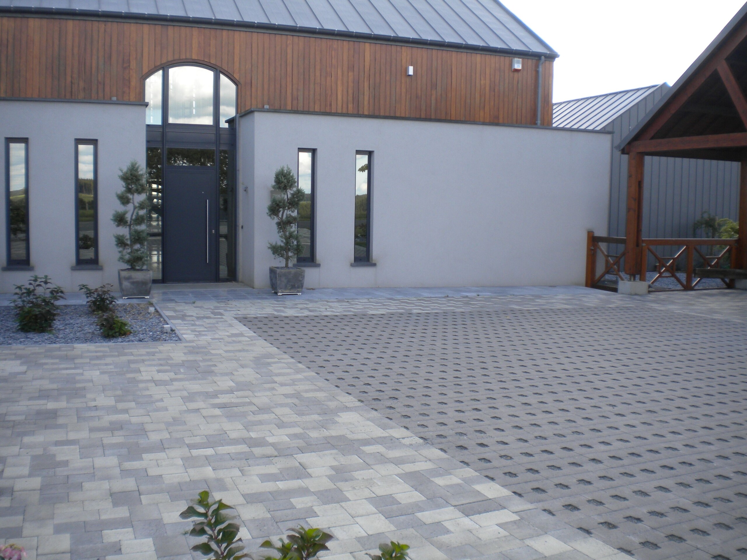 Entrée en pavés en béton devant une maison moderne avec des pots d'arbres