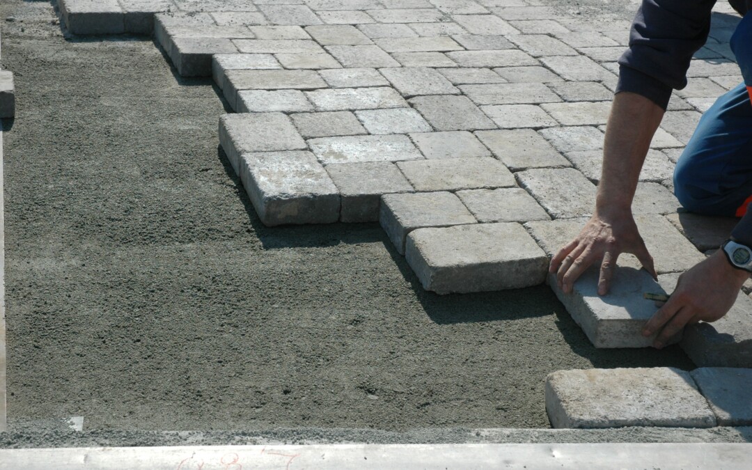 Un ouvrier en train de poser un pavé en béton gris sur du sable