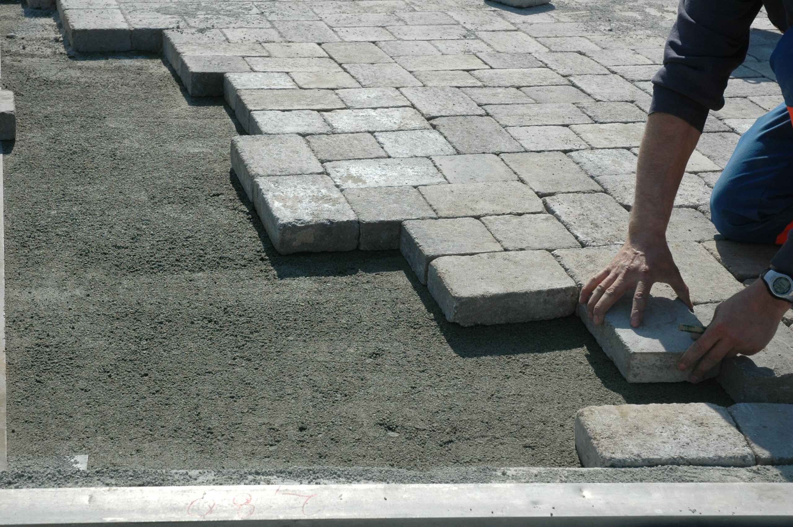 Un ouvrier en train de poser un pavé en béton gris sur du sable