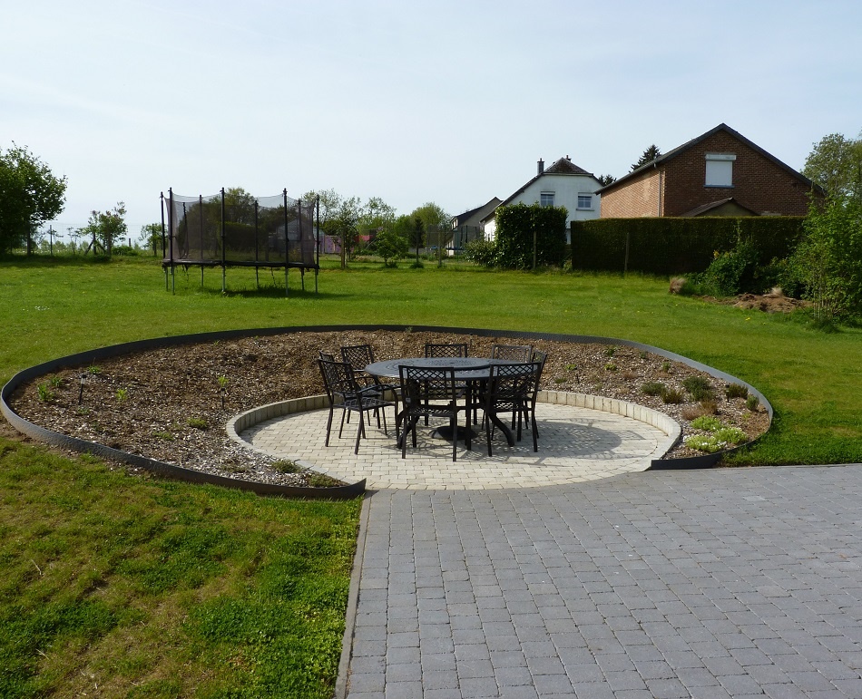 Un cercle de pavés en béton au centre d'un jardin, aménagé avec une table et des chaises en métal