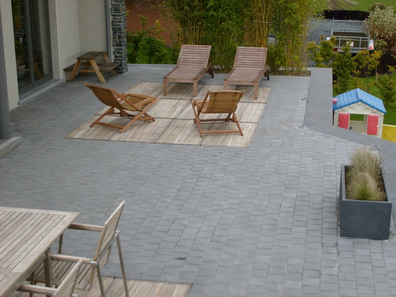 Une terrasse en béton gris avec zones en bois, aménagée avec des chaises longues et entourée de pelouse