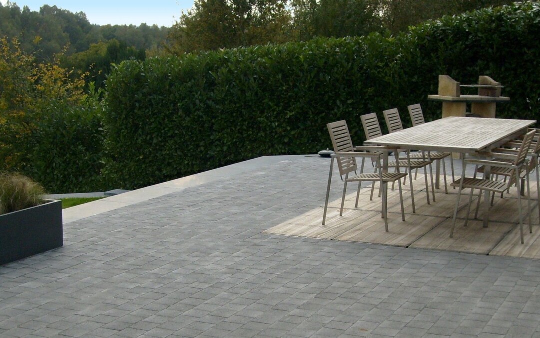 Une grande terrasse en pavés de béton gris, aménagée avec une table et des chaises