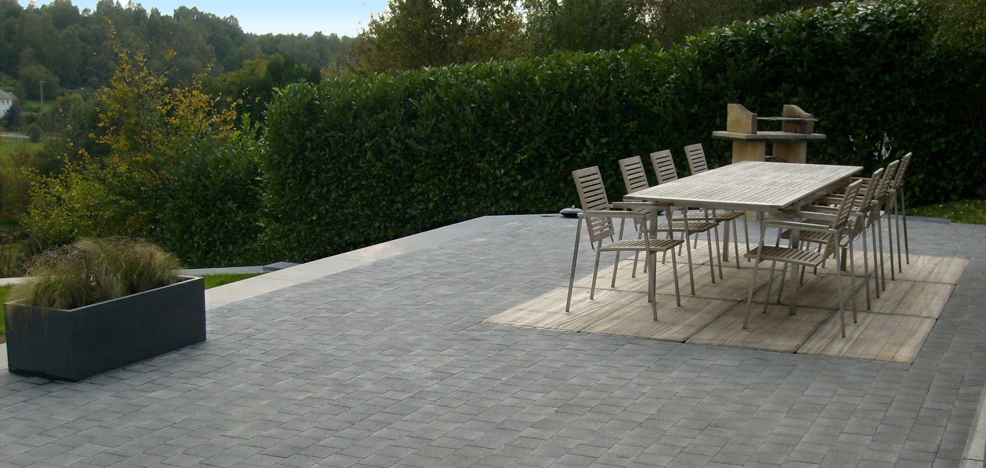 Une grande terrasse en pavés de béton gris, aménagée avec une table et des chaises