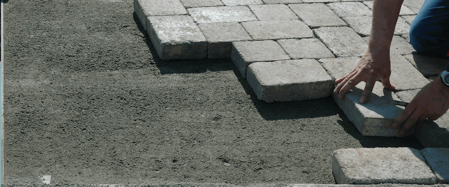 Un ouvrier pose des pavés en béton sur une couche de sable