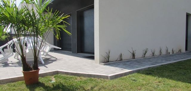 Une terrasse en béton grise bordée de pelouse